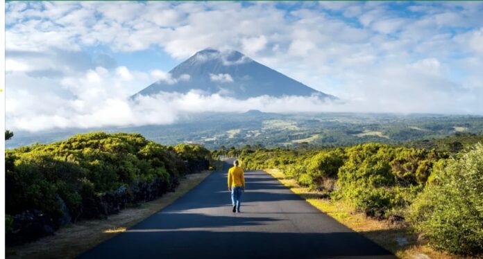 Man walking on a road surrounded by lush greenery with the majestic Pico volcano in the background in the Azores.